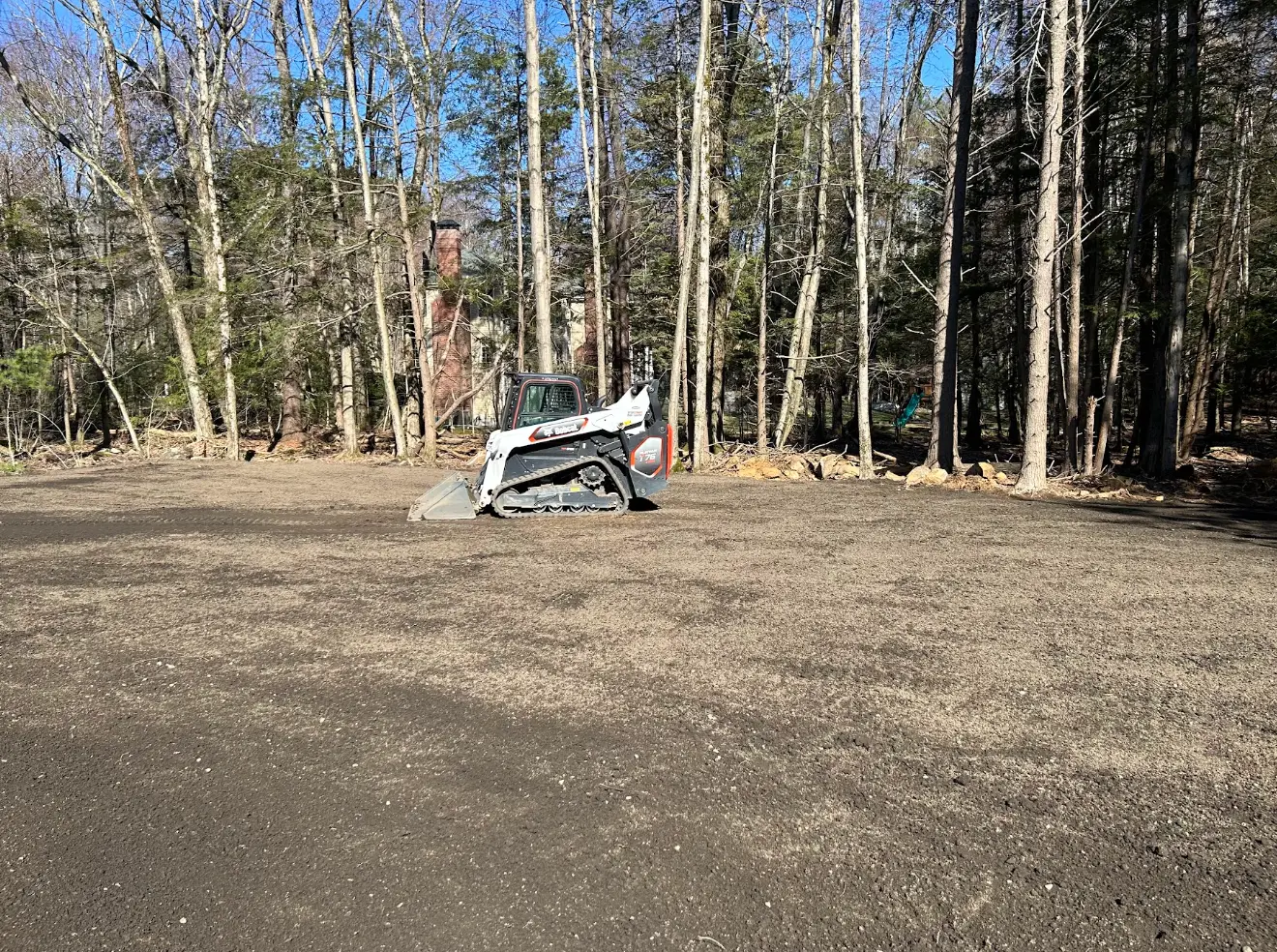 Freshly graded yard with the skid steer finishing the cleared ground